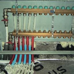 Usługi Ogólnobudowlane Daniel Wyrzykowski - Rozdzielacz instalacji grzewczej podłączony do rur w kolorach czerwonym i niebieskim, widoczne zawory i izolacja podłogowa.